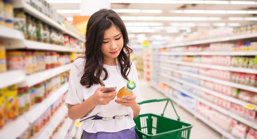 Woman in grocery store looking up a product on her phone
