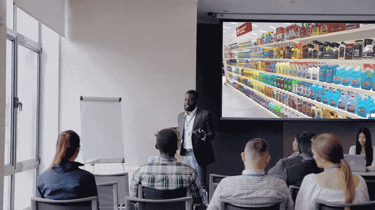Man giving retail buyer powerpoint presentation to a room of people and showing different shelf and store layouts